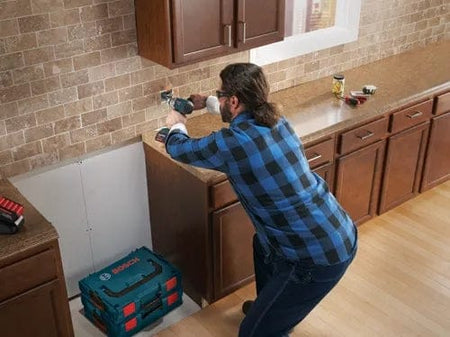 Action shot of a worker installing an outlet box in a kitchen backsplash, drilling into the tile wall with the BlueGranite bit.