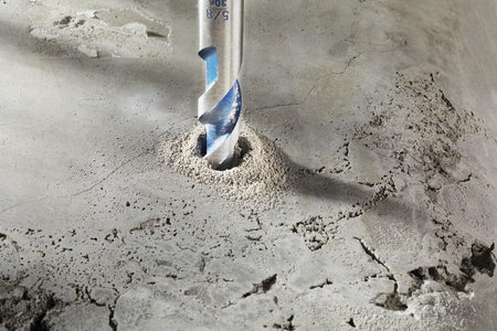 Action shot of a Bosch BlueGranite Turbo drill bit actively drilling into concrete masonry, showing dust extraction from the hole.