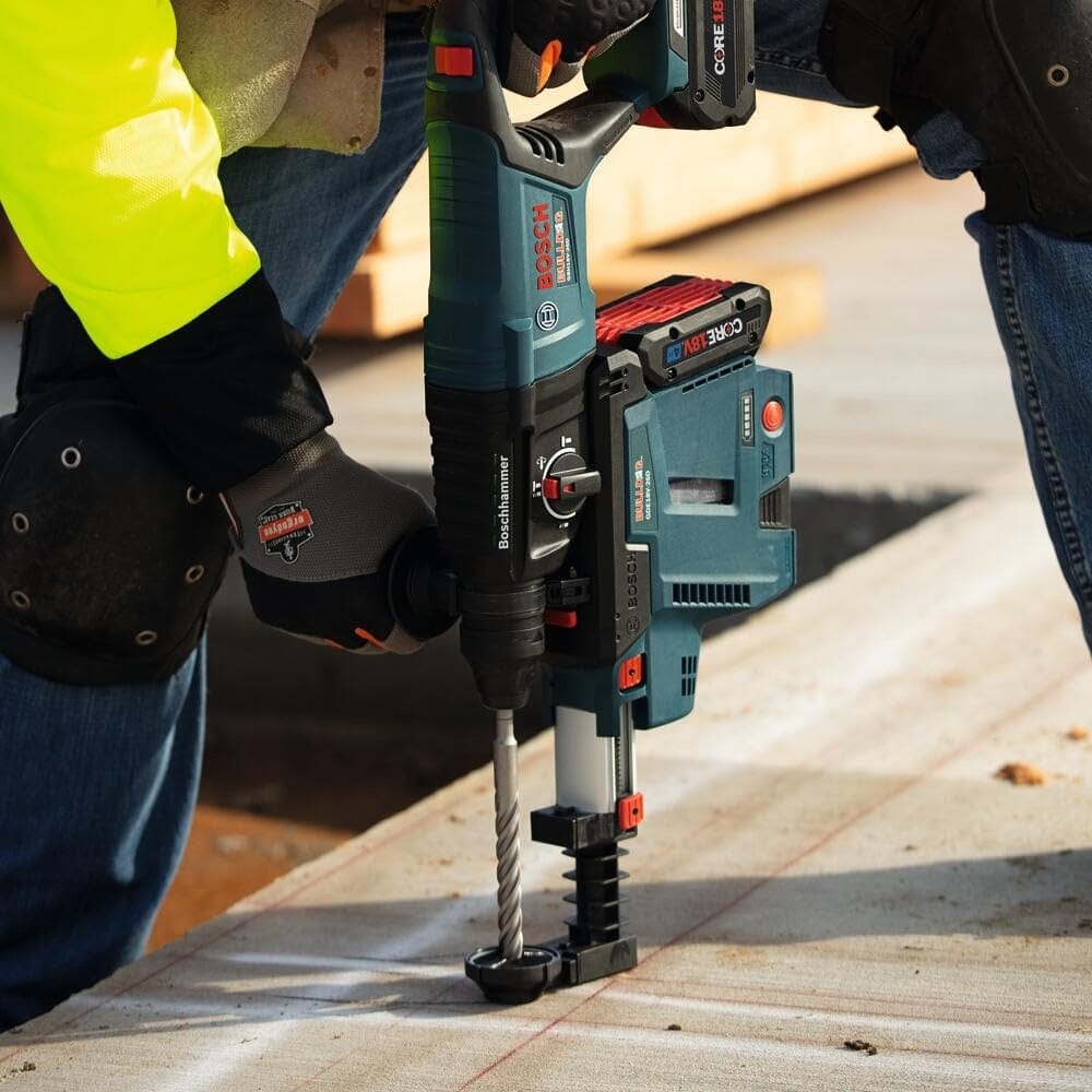 Action shot of a construction worker using a Bosch rotary hammer with a dust extractor to drill vertically into a concrete slab on a job site.