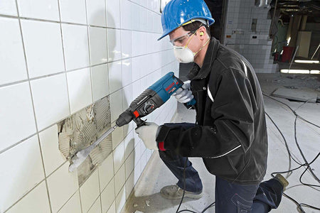 Action shot of a worker wearing a blue hard hat using the hammer only mode to chisel ceramic tiles off a wall.