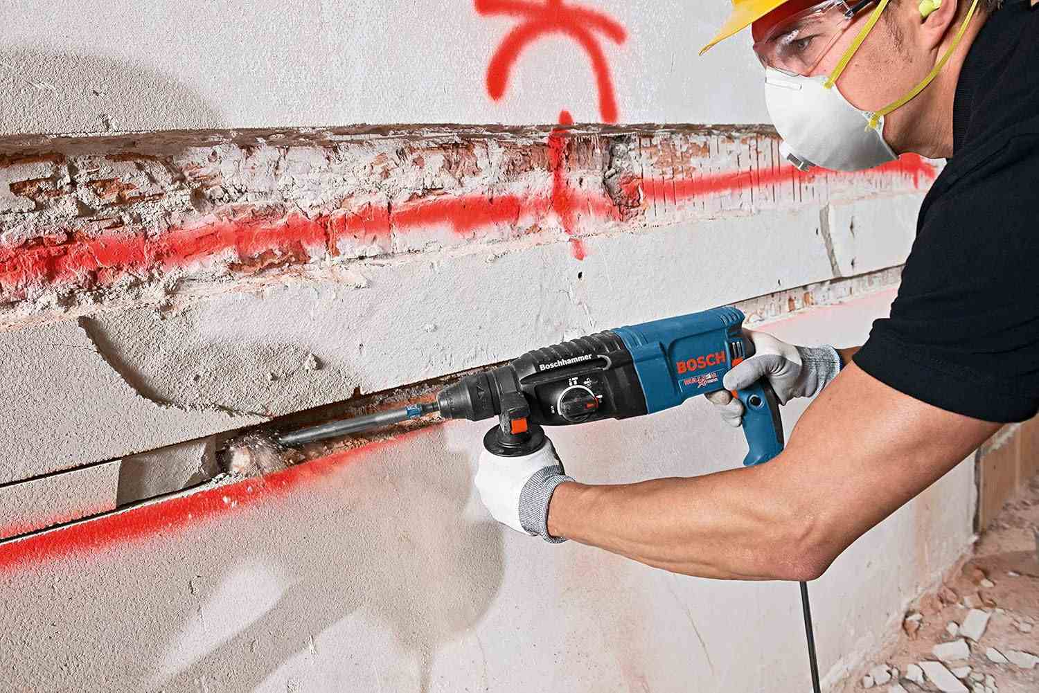 Action shot of a worker chiseling a horizontal channel into a concrete wall following a marked red line.