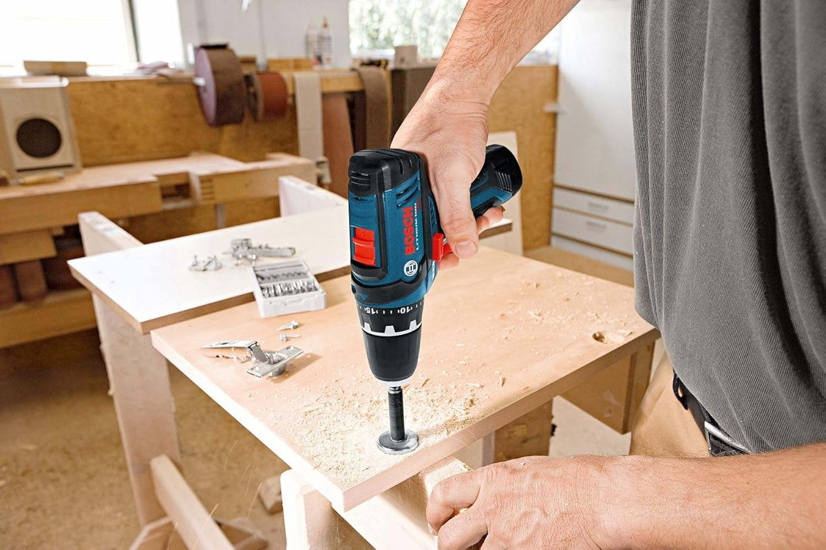 A woodworking action shot showing a person using the PS31 drill to drive a screw into the edge of a plywood sheet.