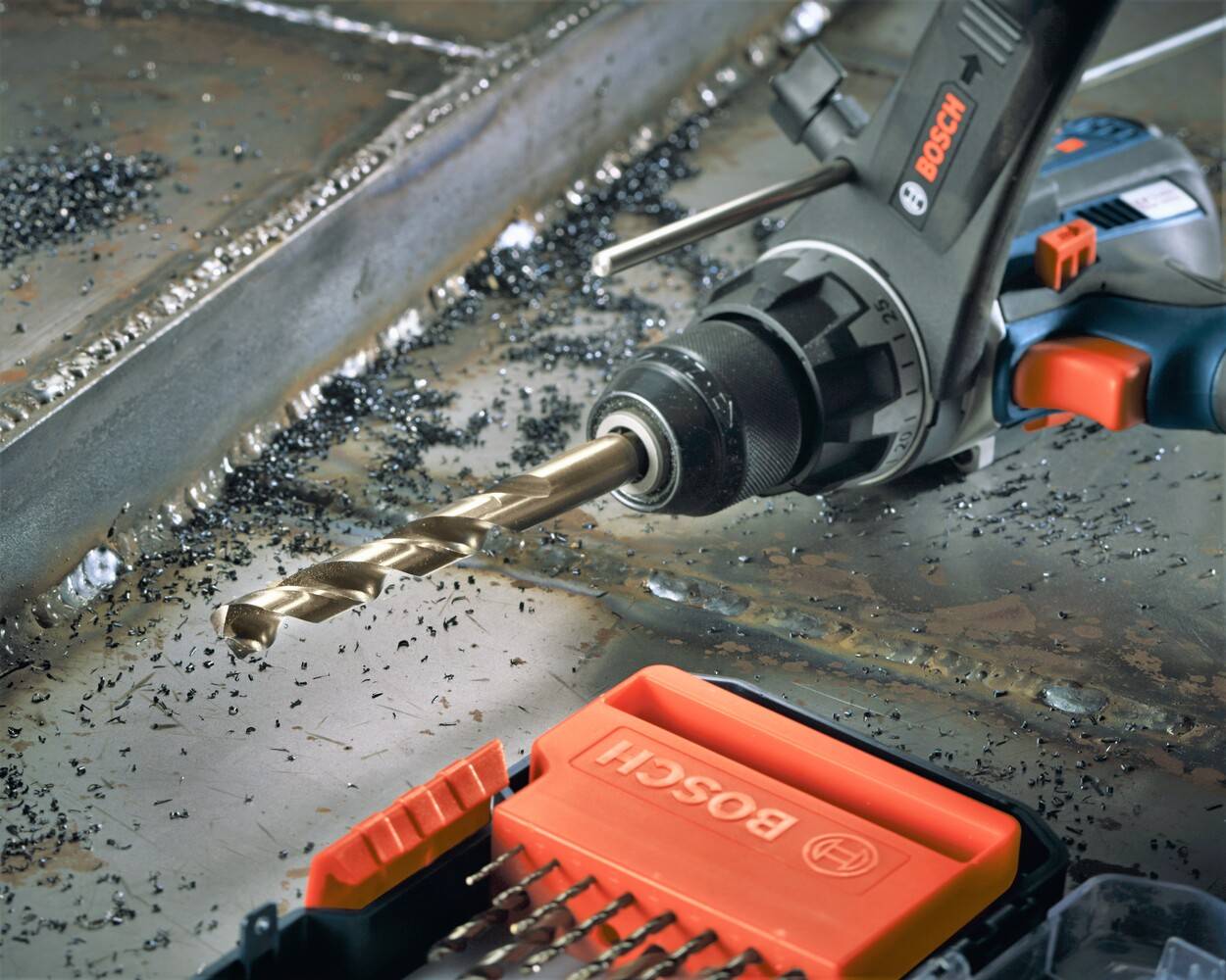 An action photograph showing a Bosch drill equipped with a cobalt M42 bit drilling into a metal surface covered in shavings, with the storage case visible in the foreground.