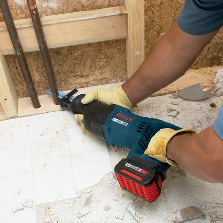 A person wearing leather work gloves using the Bosch reciprocating saw to cut through copper plumbing pipes near a wall plate.