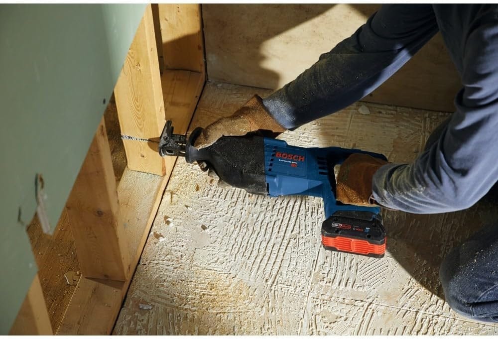 A construction worker wearing gloves using the Bosch reciprocating saw to cut through a wooden stud inside a wall cavity.
