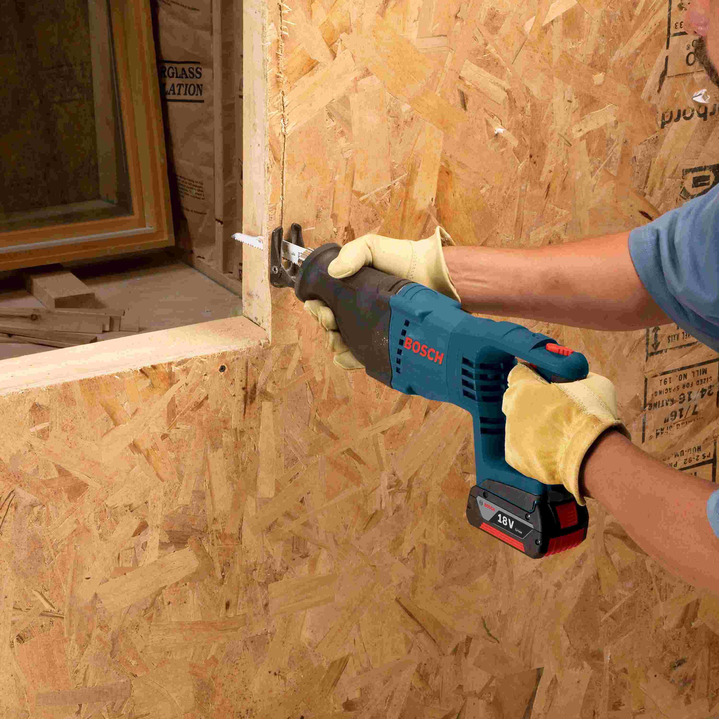 A close-up of a person using the Bosch reciprocating saw to trim a wooden frame piece during a remodeling project.