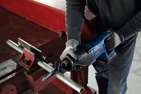 A person cutting a metal pipe secured in a vise using the Bosch reciprocating saw equipped with a metal-cutting blade.