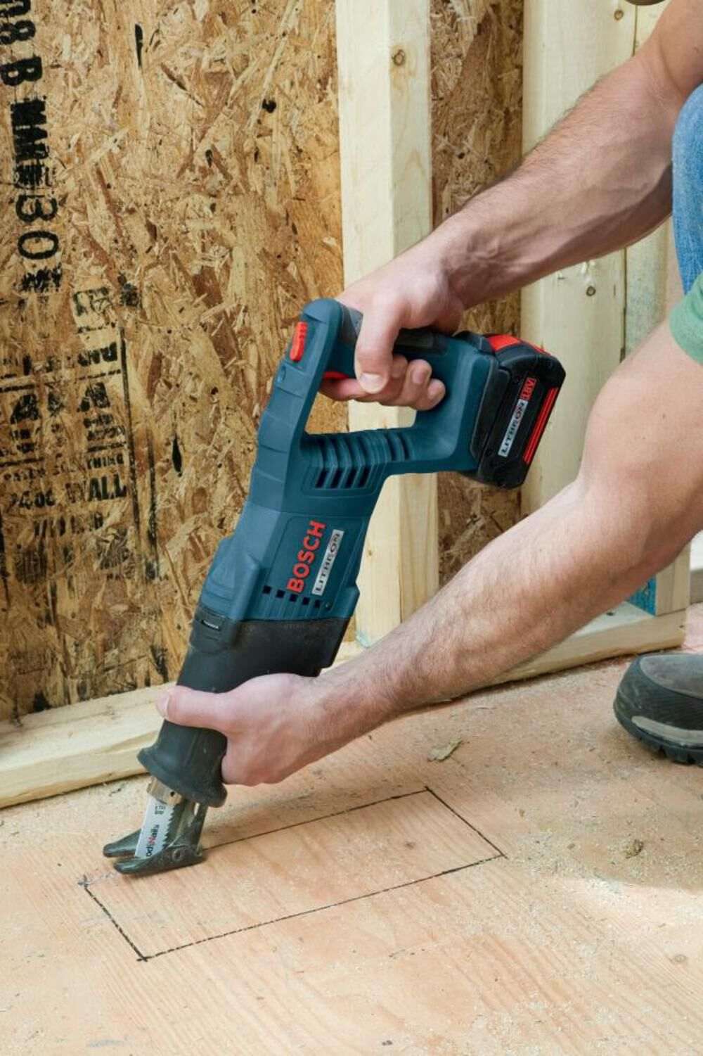 A close-up of a person holding the D-handle Bosch reciprocating saw to cut into plywood flooring.
