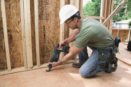A construction worker cutting a rectangular hole in a wooden floor using the Bosch 18V reciprocating saw.