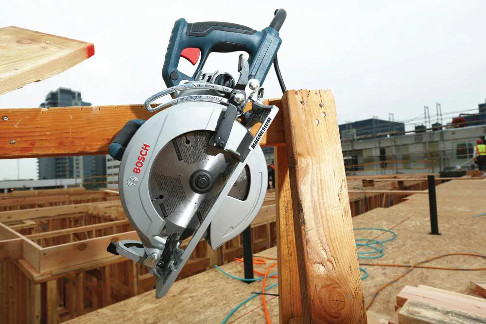 An outdoor construction application photo showing the Bosch CSW41 worm-drive circular saw stored safely by its integrated metal rafter hook, which is hanging vertically off a structural 2x4 framing lumber joist on an active residential framing deck layout.