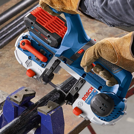 Close-up application photo of a tradesman using the Bosch GCB18V-2N 18V cordless band saw to cut a thick black steel metal pipe securely clamped inside a blue heavy-duty workshop bench vise.