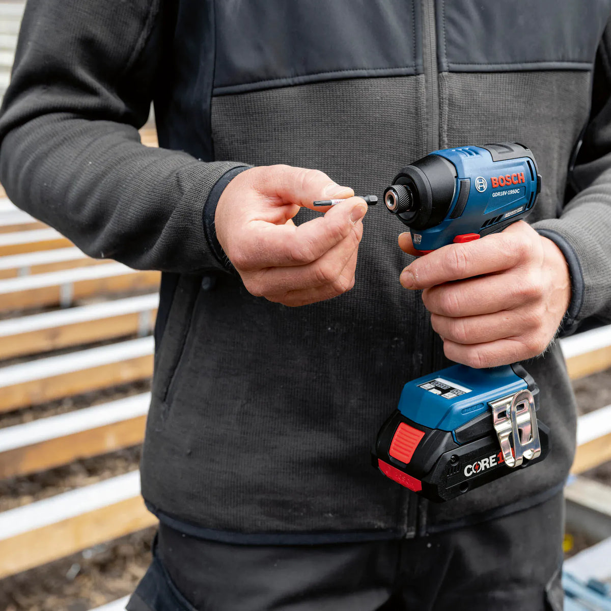 Worker inserting a hex bit one-handed into the quick-change collet of the Bosch GDR18V-1950C impact driver.