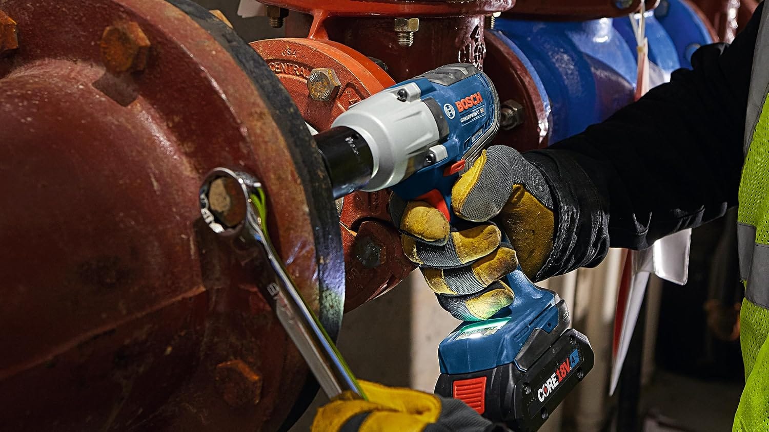 Close-up of mechanic tightening industrial pipe flange bolts with a box wrench and the Bosch 18V cordless impact wrench.