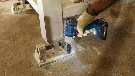 Bosch 18V impact wrench driving anchor bolts into a structural steel base plate mounted on industrial concrete flooring.