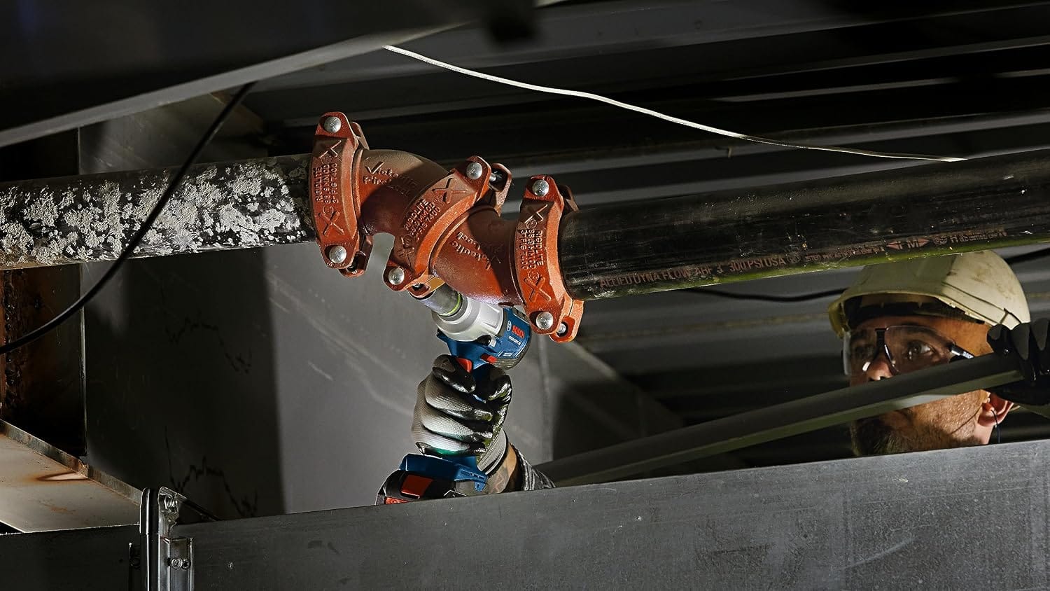Tradesperson securing overhead grooved pipe coupling bolts on a fire sprinkler line using the Bosch GDS18V-330PC.