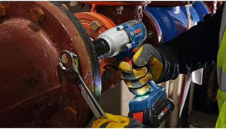 Industrial pipefitter fastening high-torque flange bolts in low light using the Bosch GDS18V-330PC impact wrench.