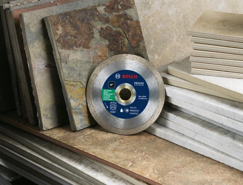 A lifestyle photograph showing the Bosch 4-inch continuous rim diamond saw blade leaning against a stack of various ceramic and stone tiles.