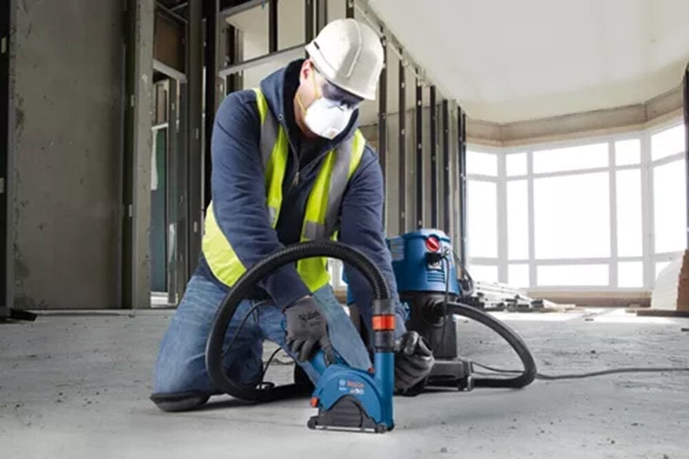 A professional construction worker in full safety gear using the Bosch DB742C diamond blade with a dust extraction system to cleanly cut through a concrete floor in a commercial renovation project.