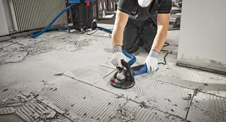 A flooring installer working on a renovation project uses an unthreaded 7/8-inch arbor diamond grinding cup wheel on a Bosch angle grinder to clear away hard thinset mortar ridges and prepare the structural concrete subfloor for new tile installation.