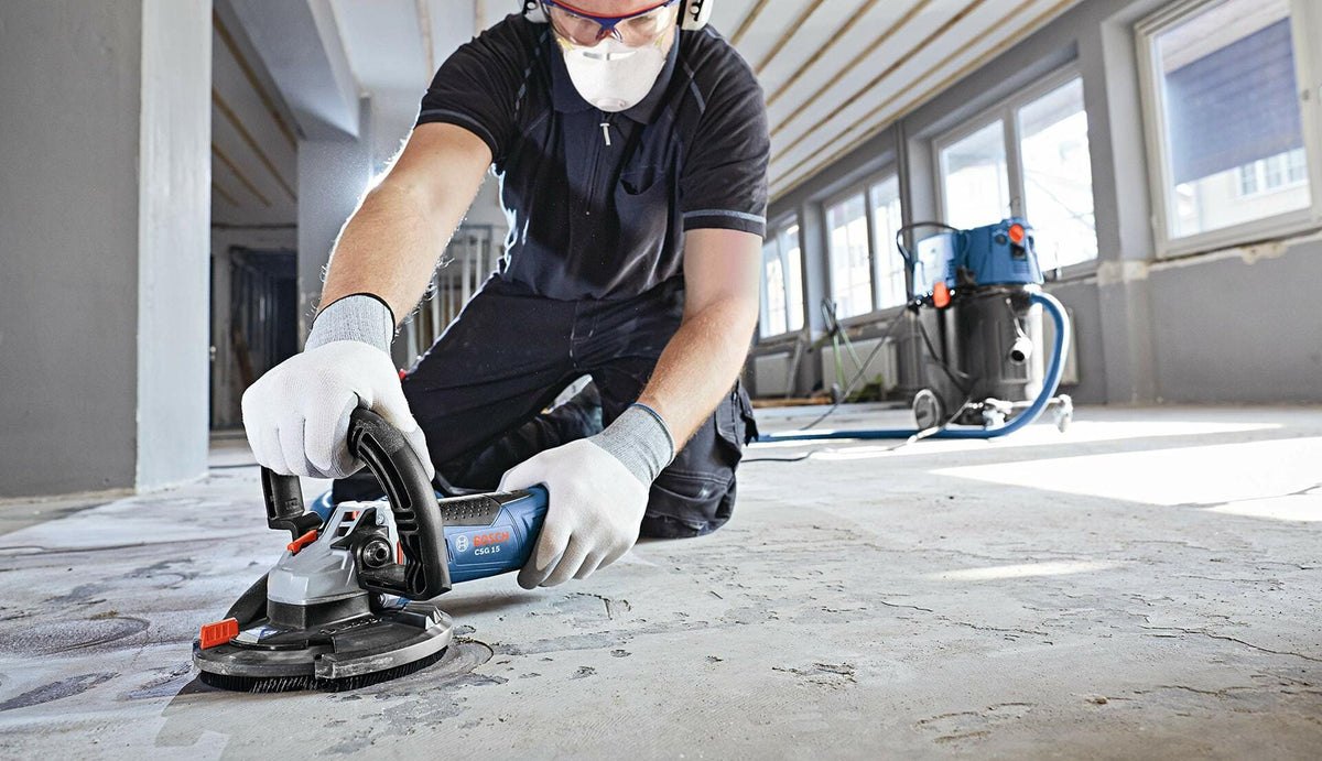 Person using BOSCH DC510HD 5 In. Double Row Segmented Diamond Cup Wheel to grind concrete floor indoors