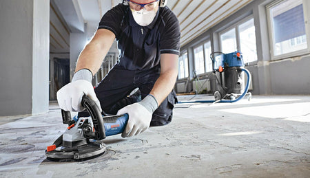 Person using BOSCH DC510HD 5 In. Double Row Segmented Diamond Cup Wheel to grind concrete floor indoors