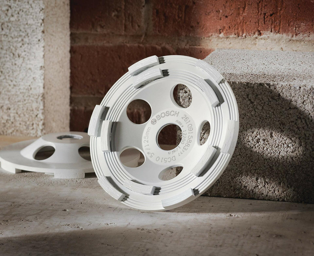 BOSCH DC510HD 5 In. Double Row Segmented Diamond Cup Wheel leaning against a concrete block on a construction site.