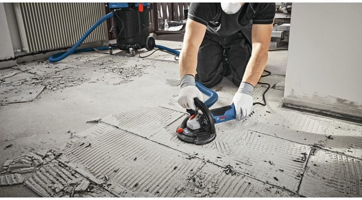 A close-up application shot of a masonry professional utilizing a 5-inch turbo-row concrete grinding disc system to aggressively scrape away old, hardened thinset mortar ridges from a concrete floor during a building renovation project.