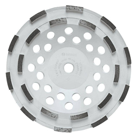 Product studio shot from a direct overhead view of the Bosch DC710H 7 Inch Double Row Segmented Rim Diamond Cup Wheel on a white background, displaying its wide white steel body, a 5/8-11 threaded center arbor hole, multiple concentric rings of round heat dissipation vents, and 12 aggressively arranged double-row segmented diamond cutting teeth.