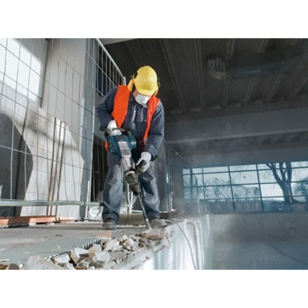 A construction worker wearing gloves and work clothes uses the Bosch DH1020VC inline SDS-Max demolition hammer to chisel a concrete floor indoors.