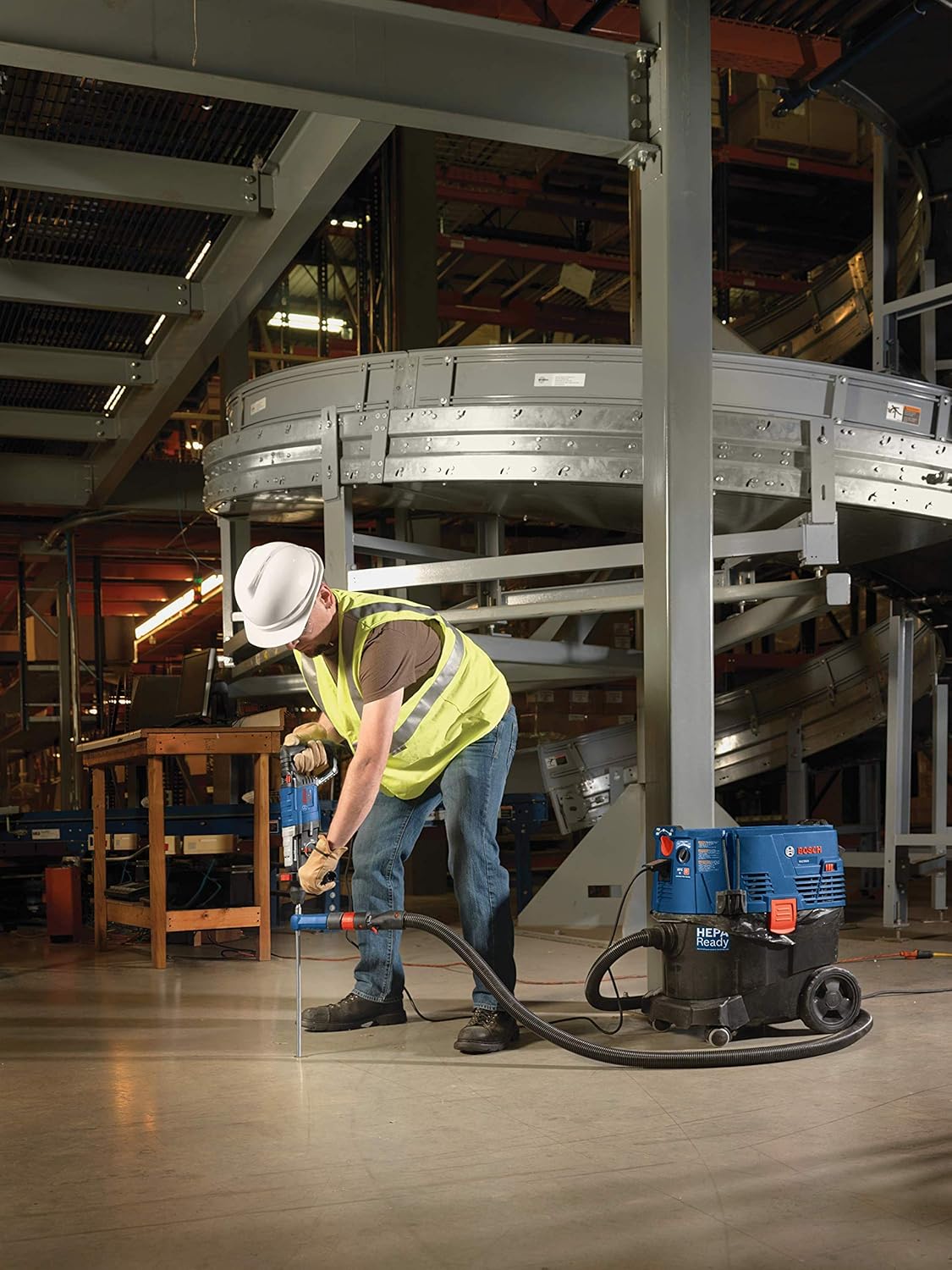A full industrial workspace view showing a contractor operating a corded Bosch hammer drill with the Speed Clean dust extraction system on a smooth concrete floor slab, illustrating how the portable HEPA-ready vacuum setup keeps the active workspace clean and free of airborne silica dust.