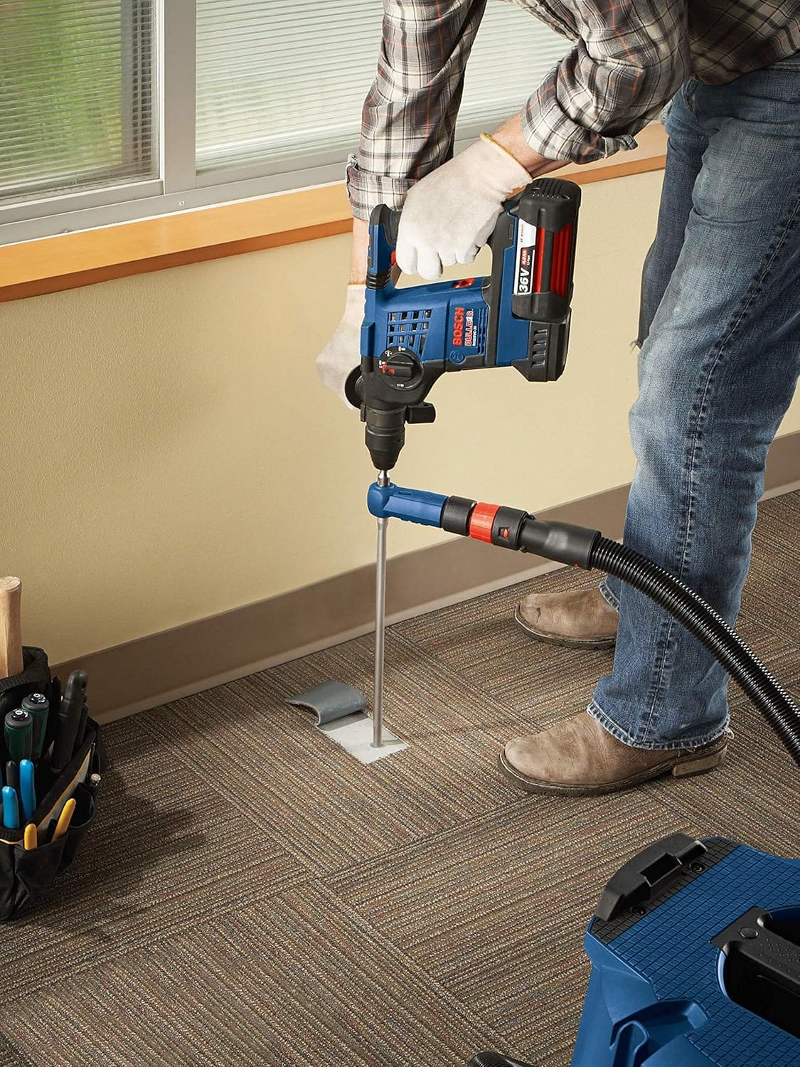 A close-up view of an installer using a cordless 36V Bosch rotary hammer drill fitted with the DXS2074 hollow suction bit to precisely drill through a carpet cutout template into the subfloor, capturing all concrete debris instantaneously to protect indoor environments.