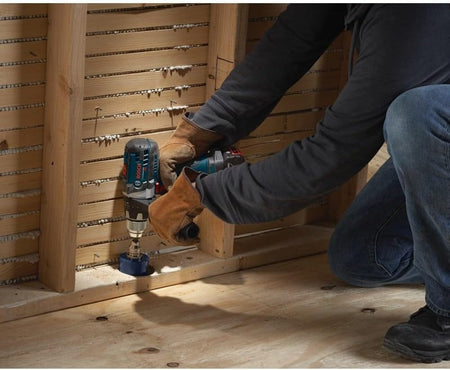 Action shot of a construction worker kneeling to drill a hole into the wooden base plate of a framed wall using the Daredevil hole saw.