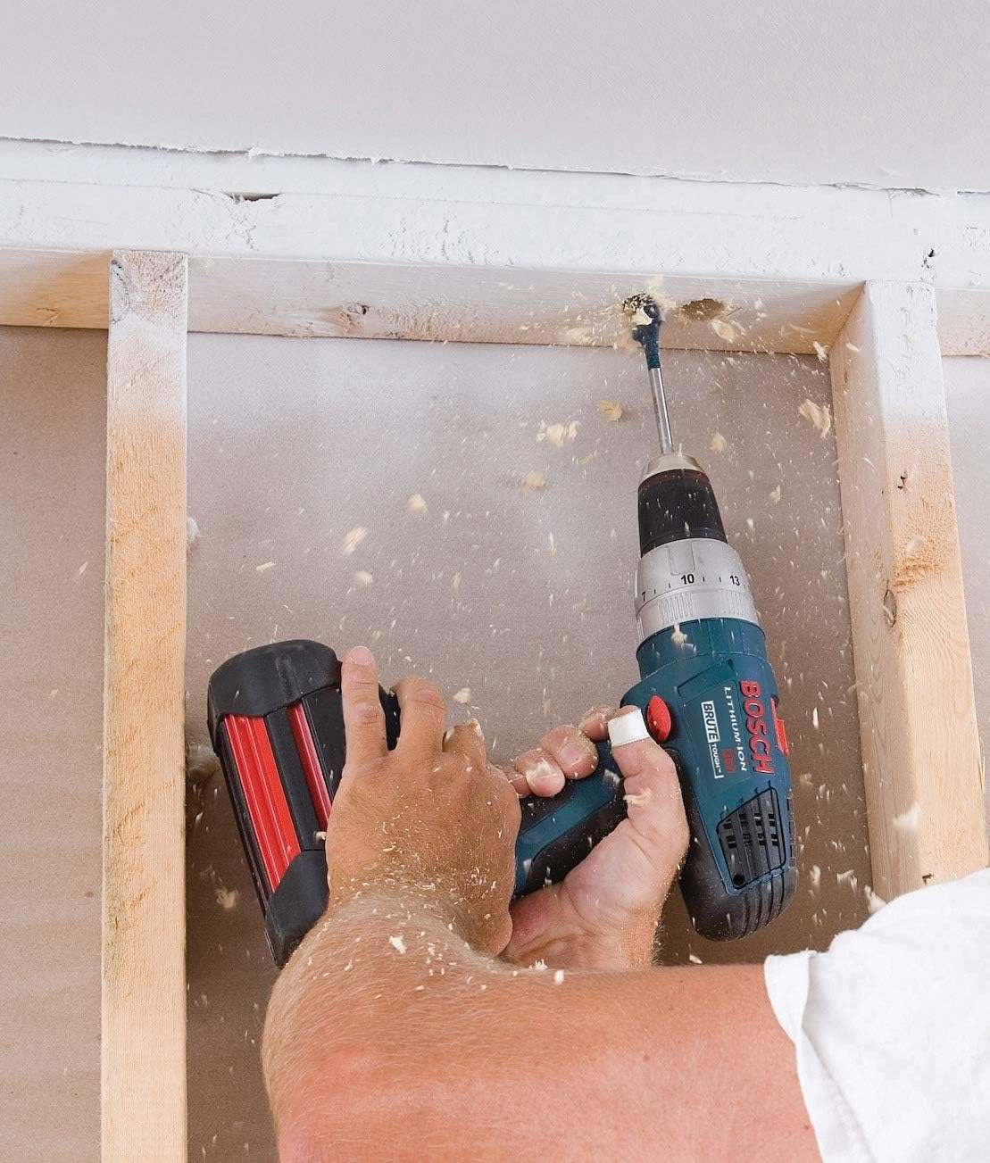Close-up action shot of the blue spade bit boring a hole through a wooden beam with wood chips being ejected by the contoured paddle.