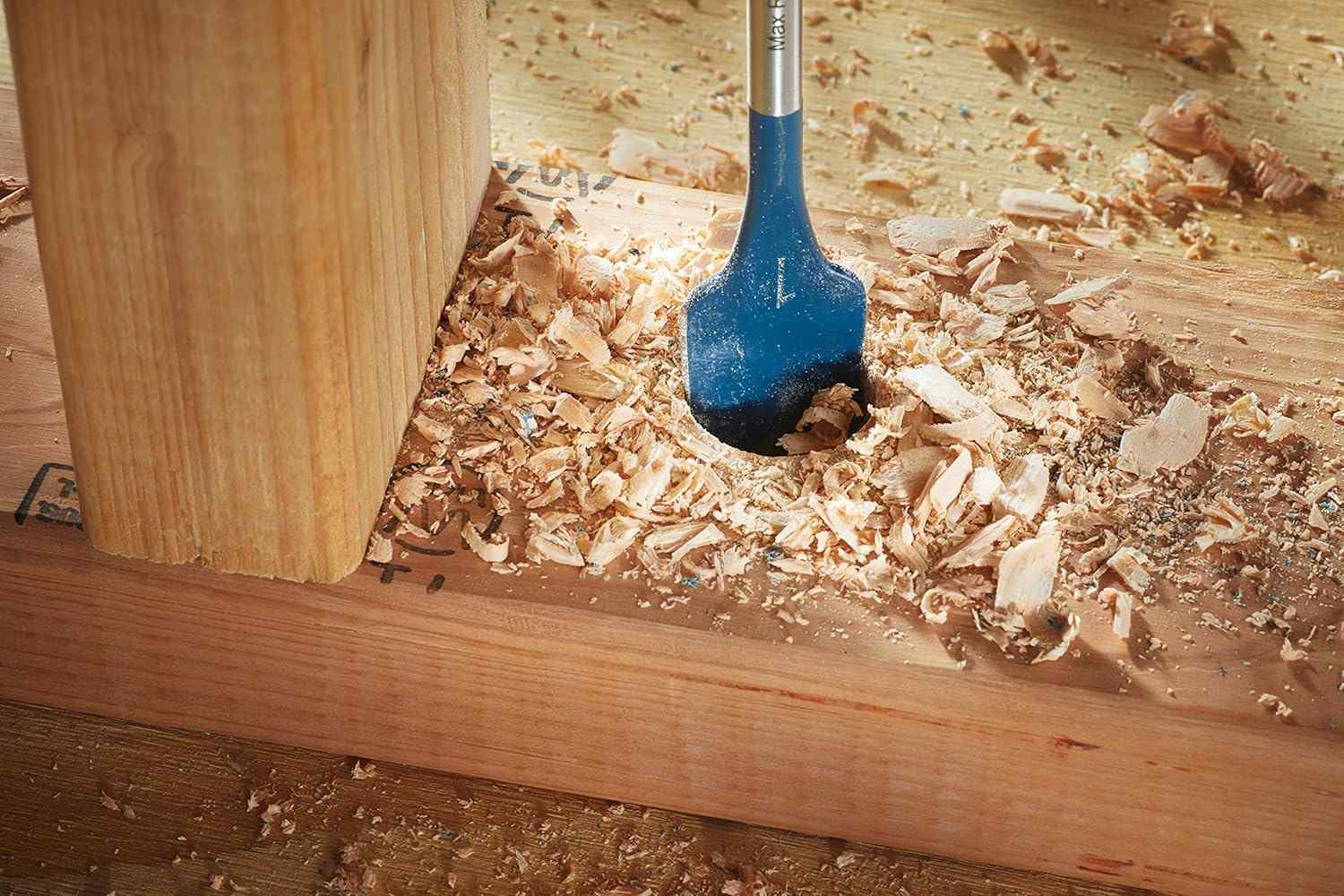 Low angle view of the spade bit secured in the chuck of a cordless impact driver with a blurred building construction background.