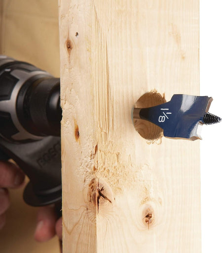 Close-up action shot of the 7/8 inch blue spade bit boring a hole through a wooden stud showing the size marking on the paddle.