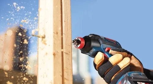 Lifestyle shot of a worker using a power drill with a spade bit to bore horizontally through a wooden framing stud.