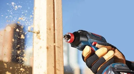 Lifestyle shot of a worker using a power drill with a spade bit to bore horizontally through a wooden framing stud.