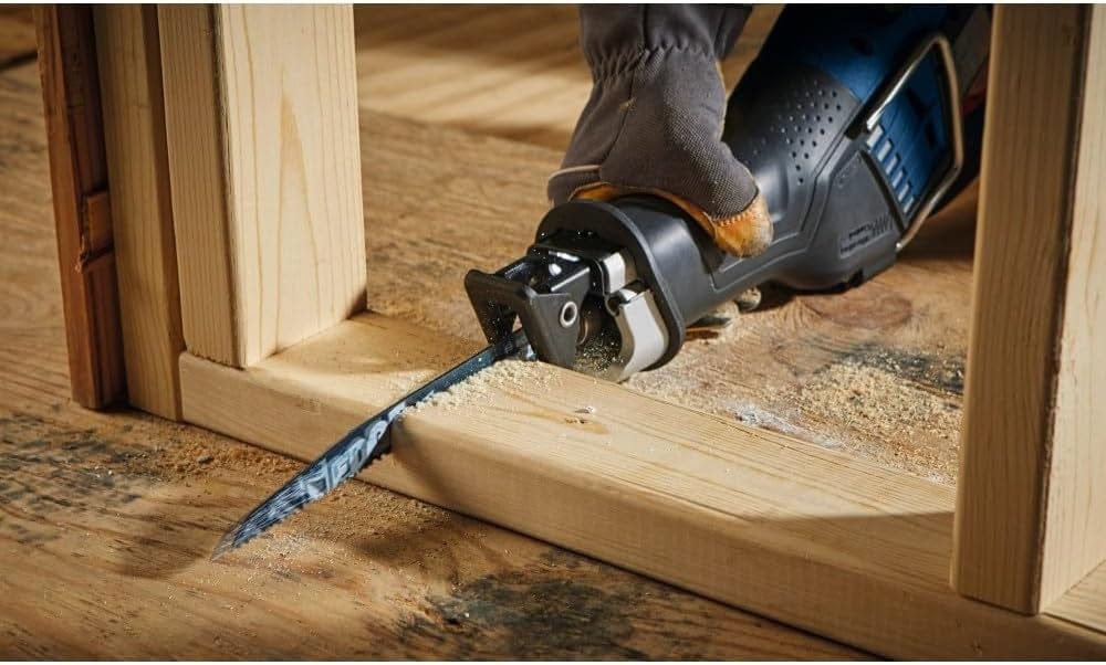 Action shot of a construction worker using the reciprocating saw to cut through wooden framing lumber near the floor.