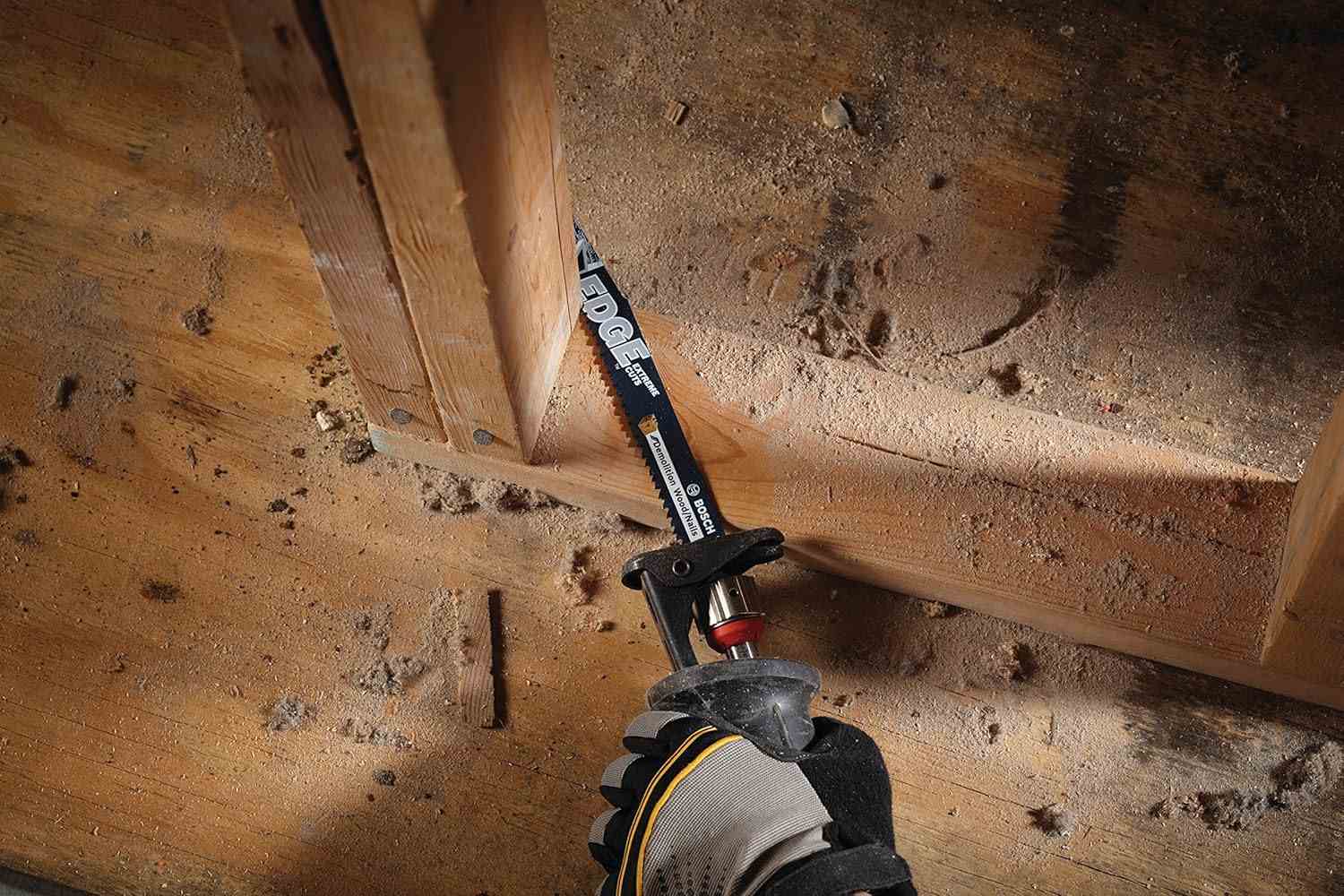 Action shot of a reciprocating saw equipped with a Bosch Edge blade cutting through the wooden base plate of a wall frame during demolition.