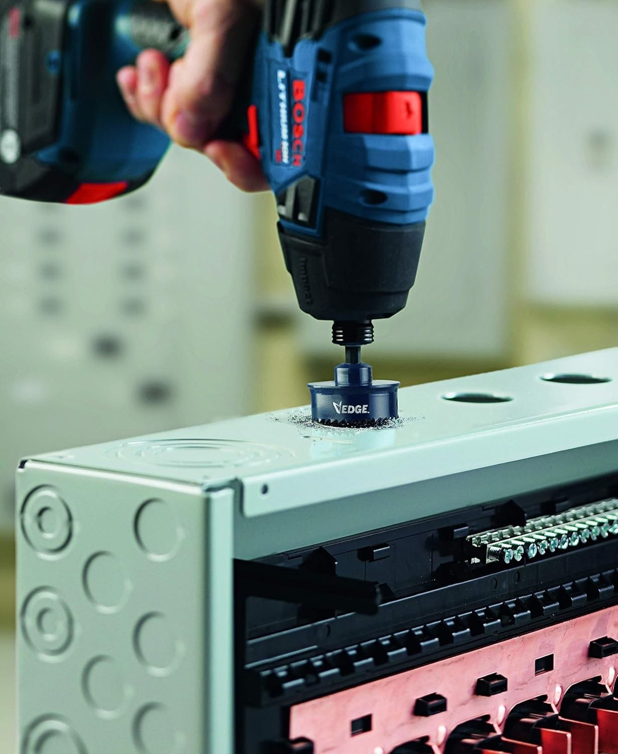 Action shot of a blue impact driver using the Edge hole saw to drill a clean hole into the top of a metal electrical box.