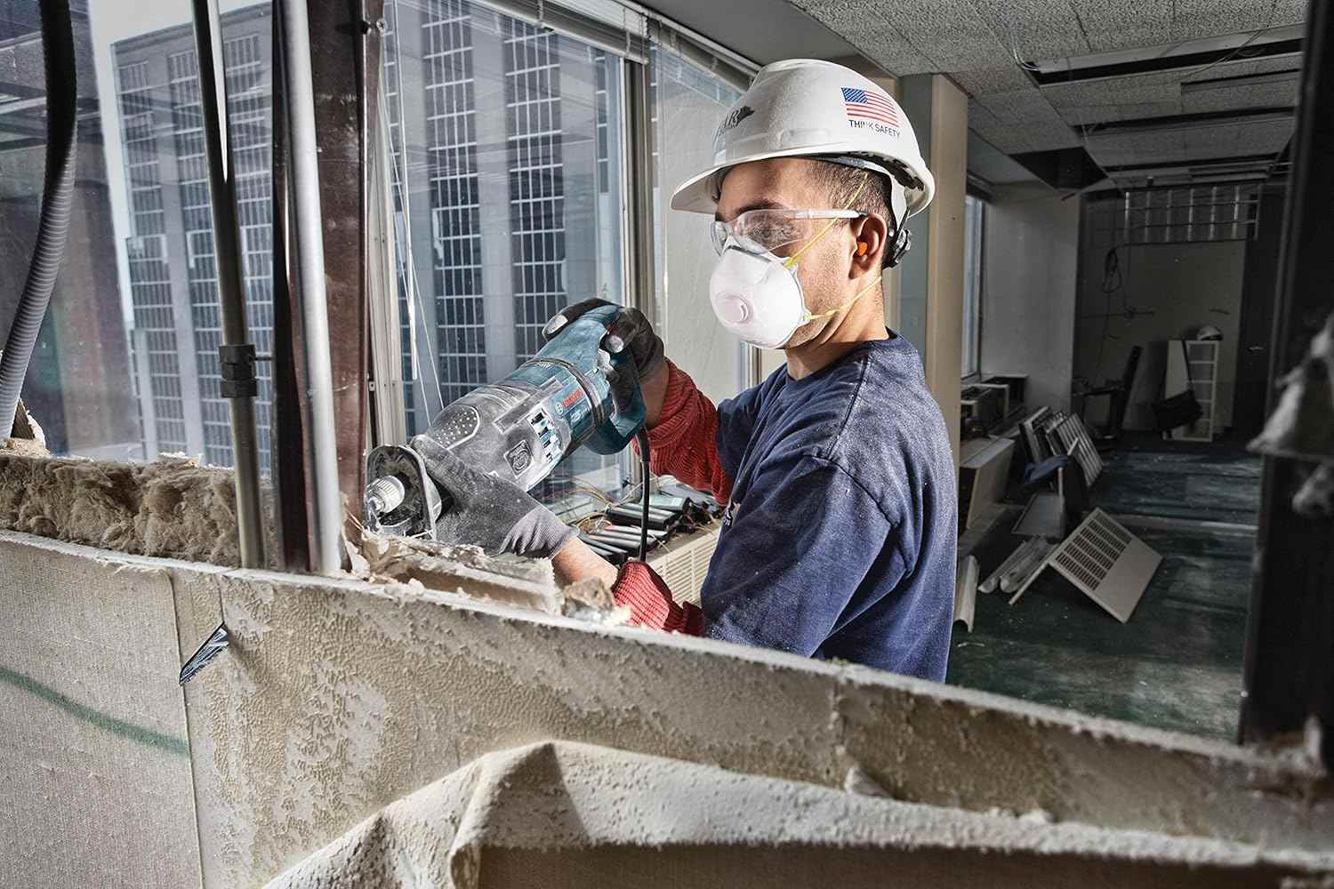 Action shot of a construction worker wearing safety gear using the reciprocating saw blade to demolish a wall section in a commercial space.