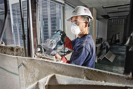 Action shot of a construction worker wearing safety gear using the reciprocating saw blade to demolish a wall section in a commercial space.