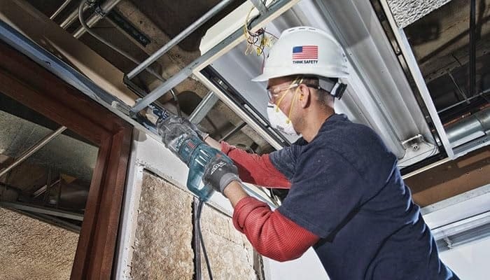 Low angle action shot of a worker using the blade to cut through overhead metal door framing during a renovation project.
