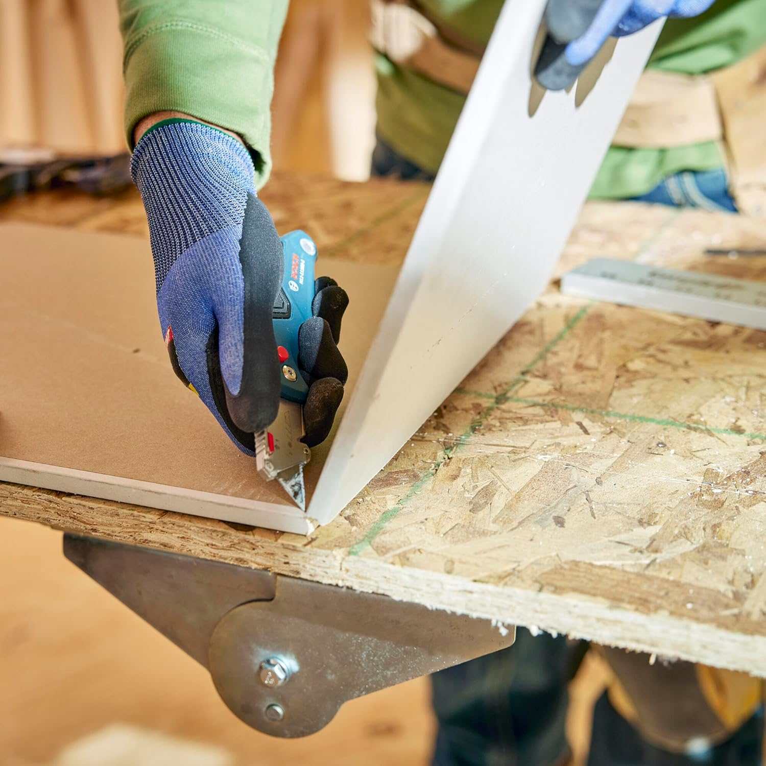 Action shot of a gloved user cutting a piece of drywall with the utility knife, demonstrating the use of the thumb rest for added pressure and control.