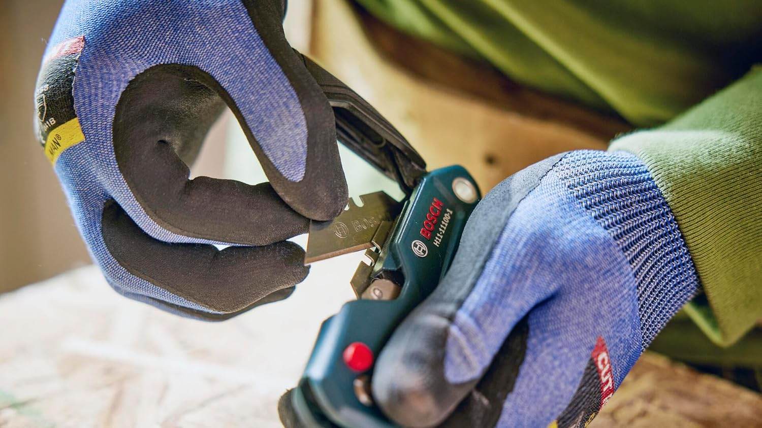 Close-up of gloved hands demonstrating the tool-free blade change by pressing the release button to remove the utility blade.