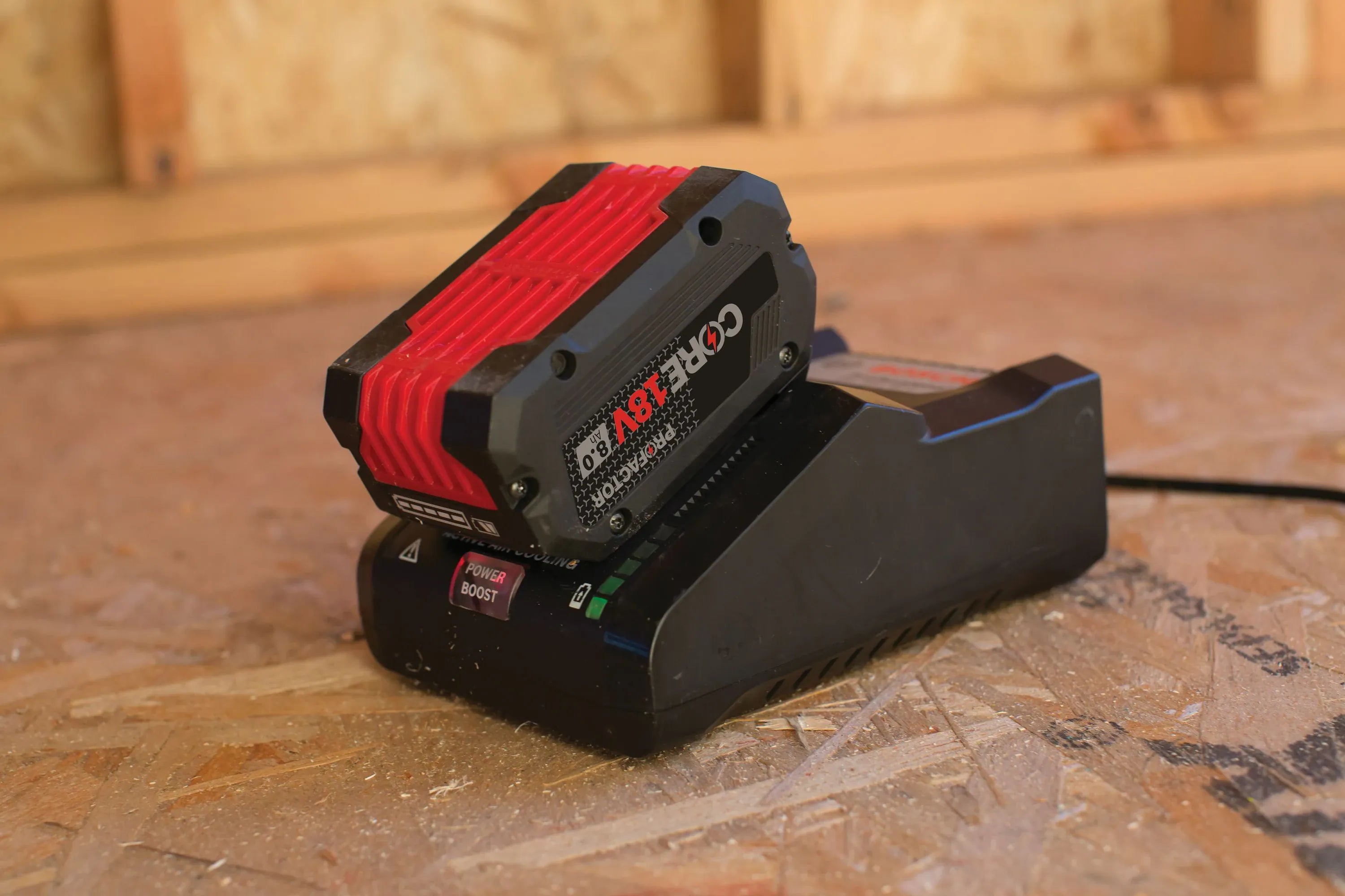 The Bosch 16 Amp turbo charger in a real-world jobsite setting, charging a CORE18V High Power battery on a wooden subfloor to demonstrate its rugged professional performance.