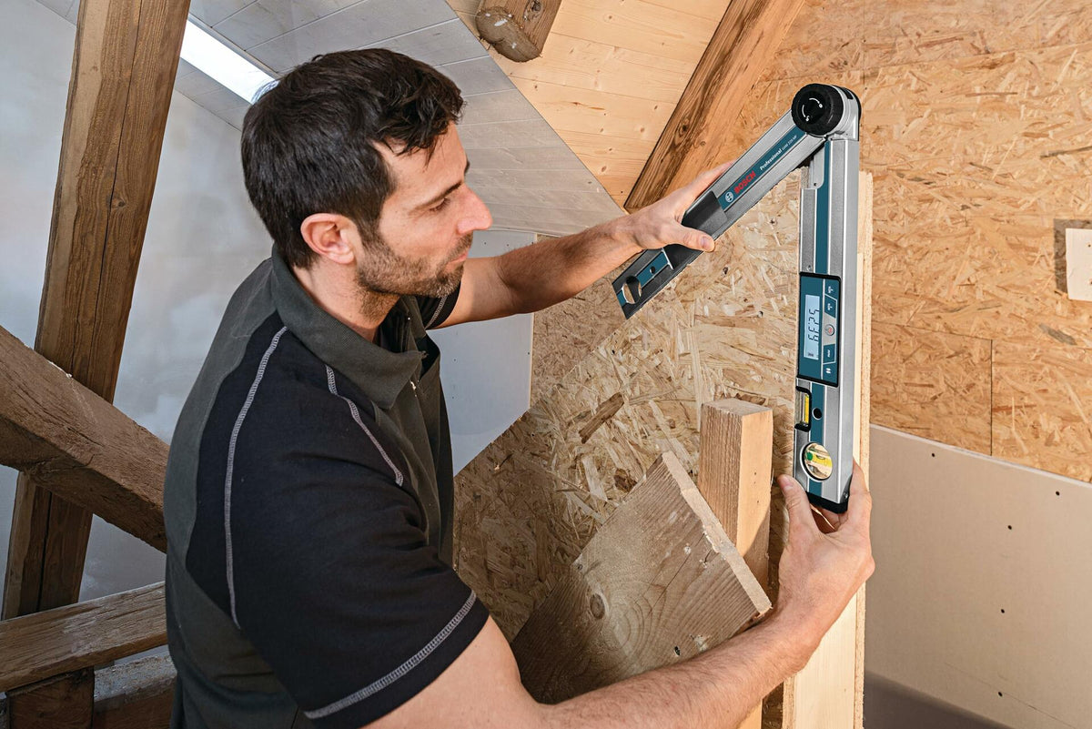 Worker measuring an acute vertical corner angle in rough construction framing using the Bosch GAM 220 MF digital angle finder, with the illuminated display showing 66.25