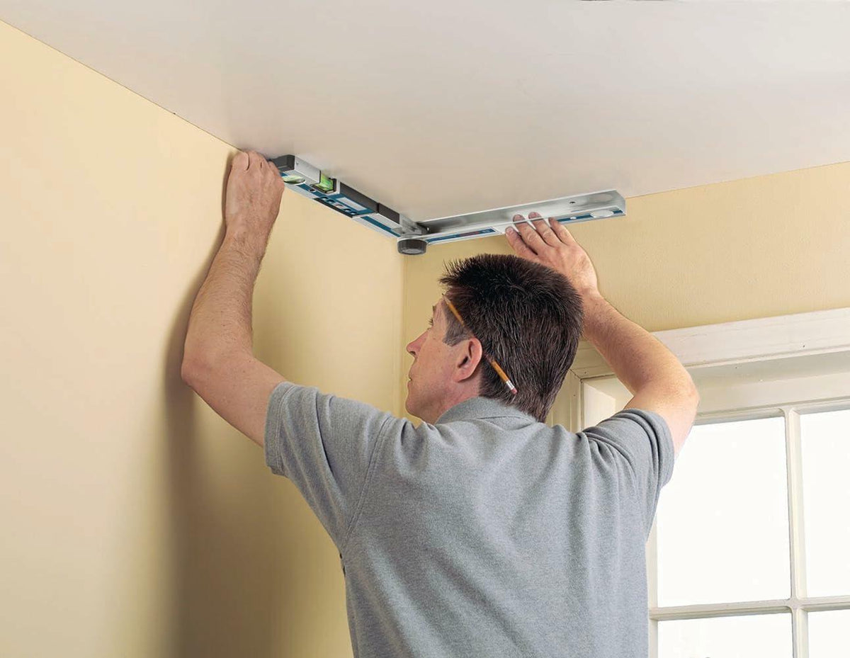Worker holding the Bosch GAM 220 MF angle finder overhead to measure an inner ceiling corner angle for precise crown molding installation