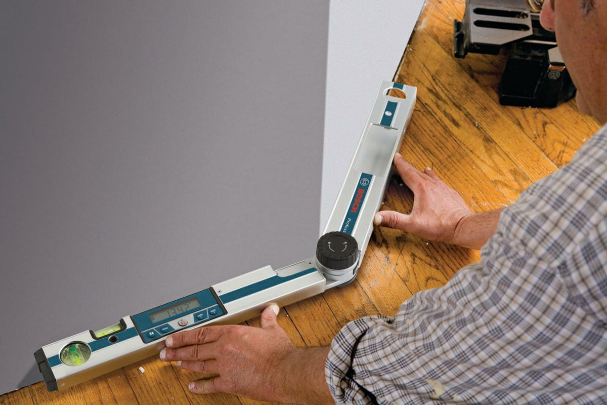 Worker using the Bosch GAM 220 MF digital angle finder to measure a wide 134.2 angle at the wall-to-floor joint for baseboard or flooring installation