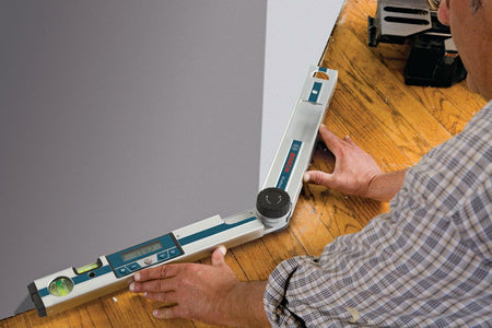 Worker using the Bosch GAM 220 MF digital angle finder to measure a wide 134.2 angle at the wall-to-floor joint for baseboard or flooring installation